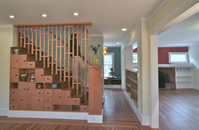 An interior photo looking at the side of a stair, with a wood screen above and many built-in cabinet doors and display nooks below.